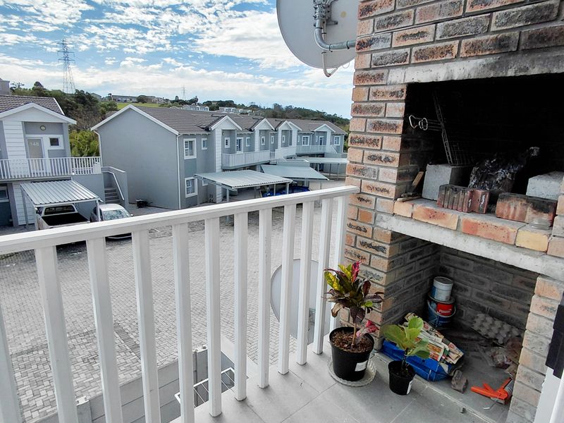 A balcony featuring a built-in brick braai, tiled flooring, and a metal balustrade, overlooking the apartment complex parking area.