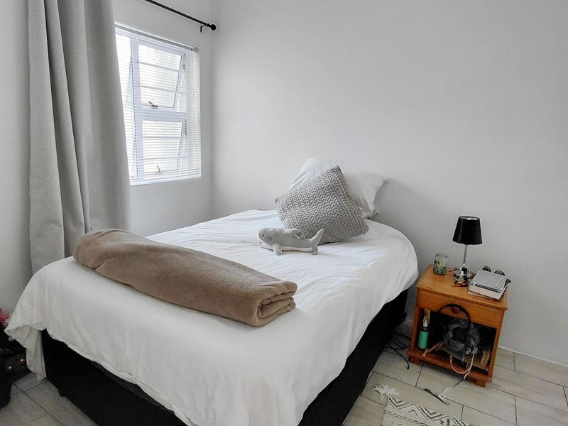 A clean and simple bedroom featuring tiled flooring and a louvered window with neutral curtains.