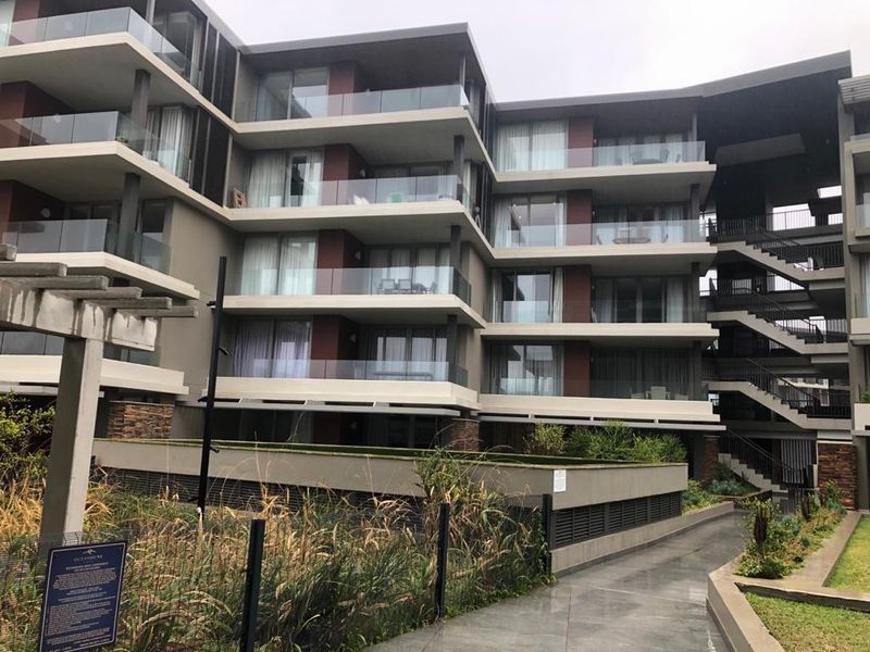 Modern multi-story apartment complex featuring contemporary architecture with glass-fronted balconies, external staircases, and landscaped ground-level garden areas.