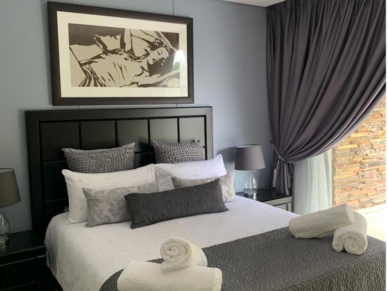 A well-maintained bedroom featuring neutral wall tones, recessed downlighting, and direct access to an outdoor area with stone feature walling.