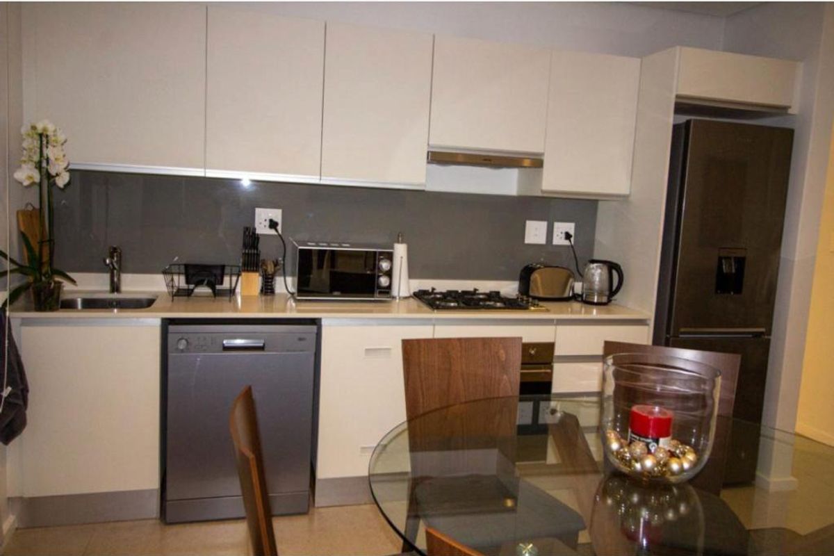Modern kitchen featuring sleek white cabinetry, stone countertops, a glass splashback, and integrated stainless steel appliances including a gas hob and oven.