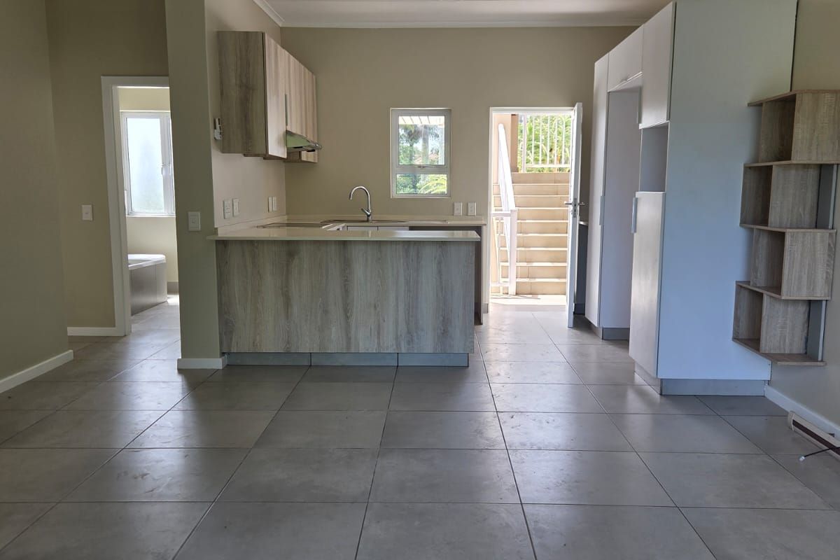 Open plan kitchen featuring light wood-look cabinetry, stone countertops, and tiled flooring, with direct access to an exterior staircase.