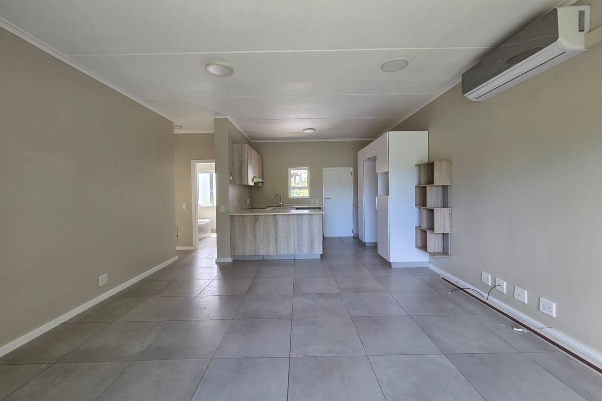 Open-plan living area featuring large format floor tiles, a modern kitchen with wood-look cabinetry, and a wall-mounted air conditioning unit.
