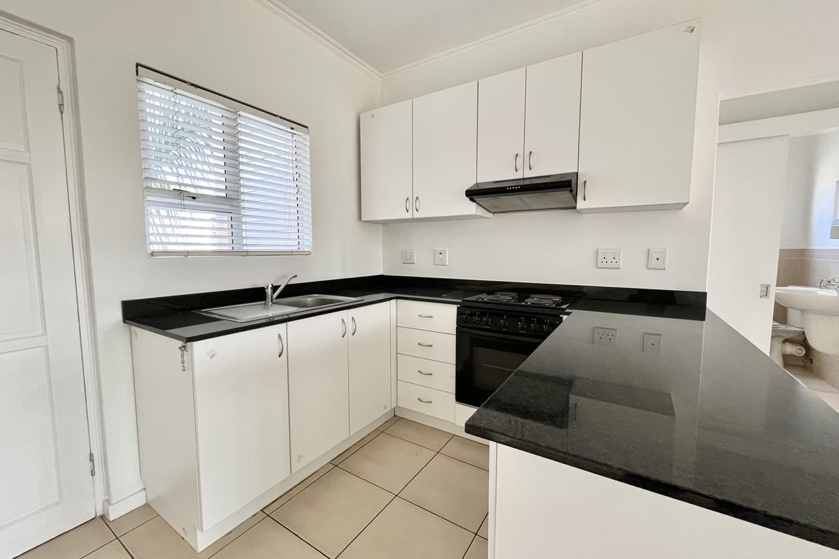 A clean, functional kitchen featuring white cabinetry, contrasting black granite countertops, built-in oven with hob, and tiled flooring.