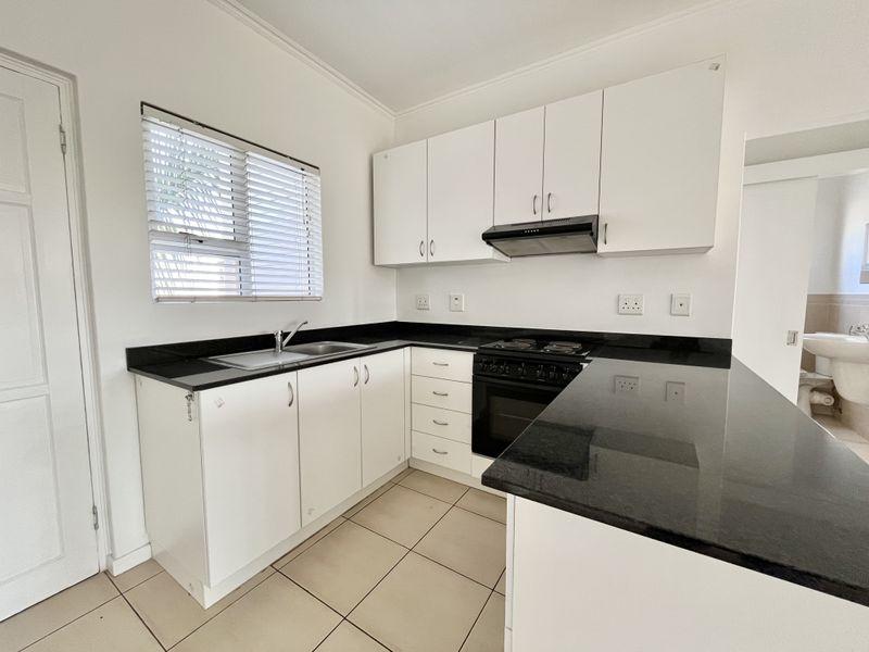 A clean, functional kitchen featuring white cabinetry, contrasting black granite countertops, built-in oven with hob, and tiled flooring.
