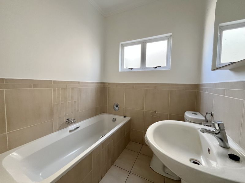 A clean, functional bathroom featuring a bathtub, pedestal basin, and toilet with neutral wall and floor tiling.