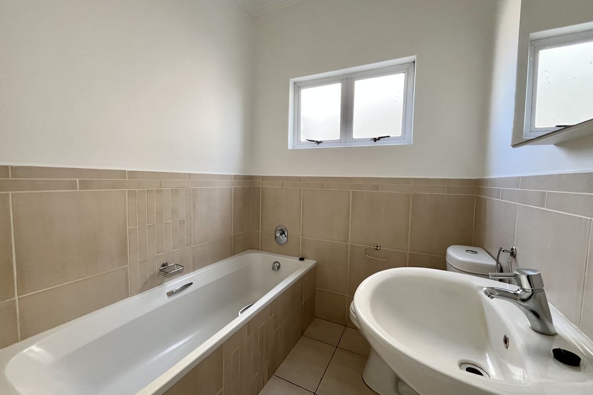 A clean, functional bathroom featuring a bathtub, pedestal basin, and toilet with neutral wall and floor tiling.