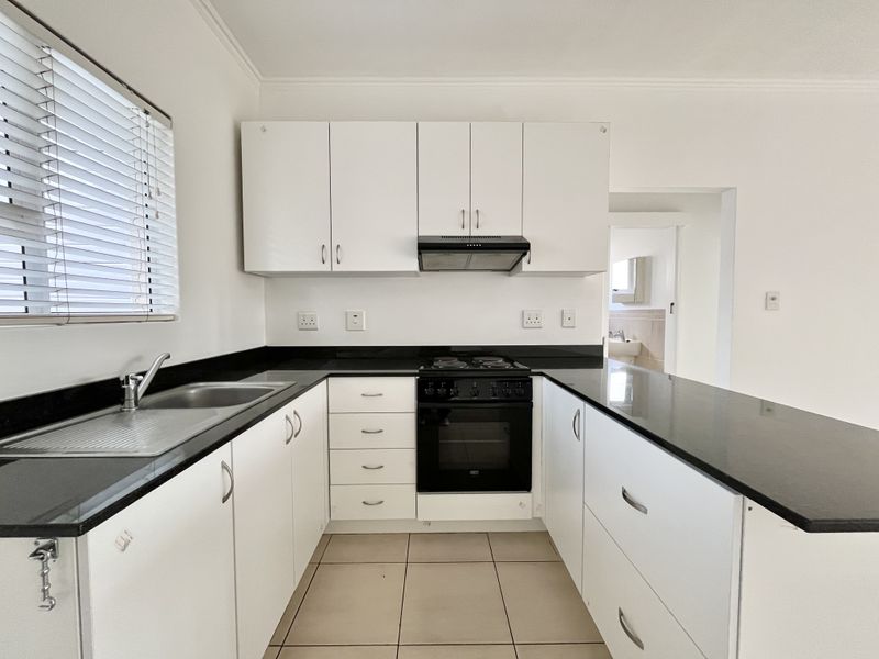 A clean, functional kitchen featuring white cabinetry, black granite countertops, a built-in oven with hob, and tiled flooring.