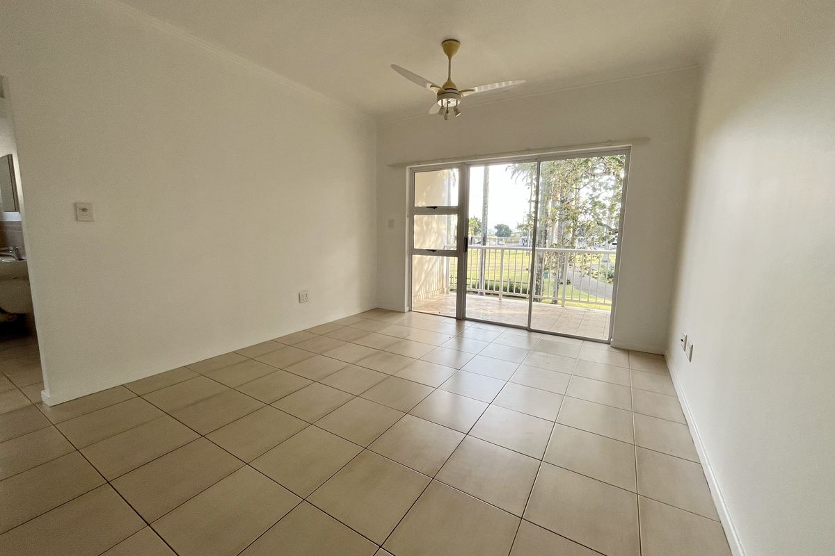 An empty living room featuring neutral tiled flooring, a ceiling fan, and large sliding glass doors providing access to an outdoor balcony area.