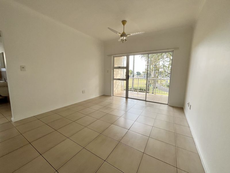An empty living room featuring neutral tiled flooring, a ceiling fan, and large sliding glass doors providing access to an outdoor balcony area.