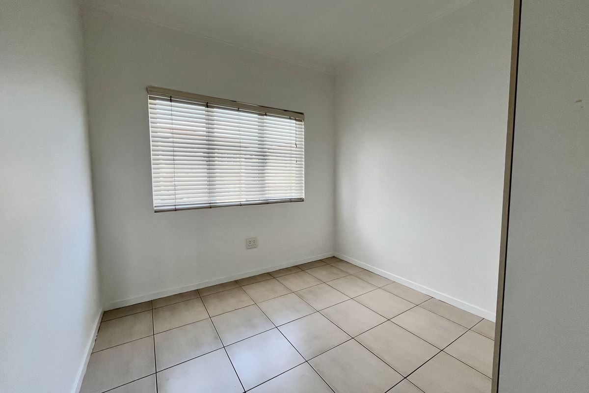 A clean, empty bedroom featuring neutral tiled flooring and fitted venetian blinds, providing a blank canvas for personalization.