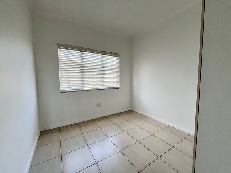 A clean, empty bedroom featuring neutral tiled flooring and fitted venetian blinds, providing a blank canvas for personalization.