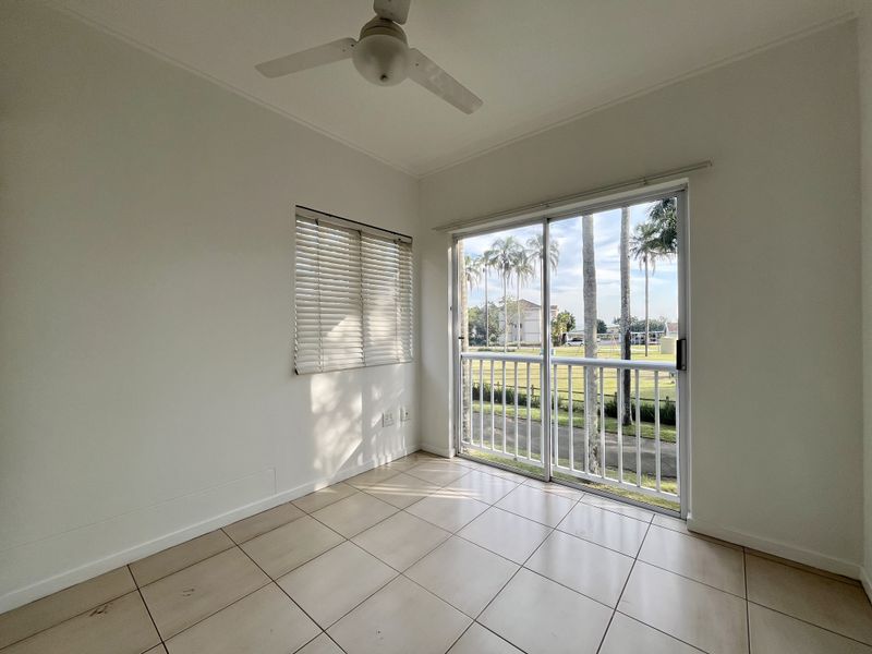 A bright, empty bedroom featuring tiled flooring, a ceiling fan, and a sliding glass door that opens to a balcony with scenic views.