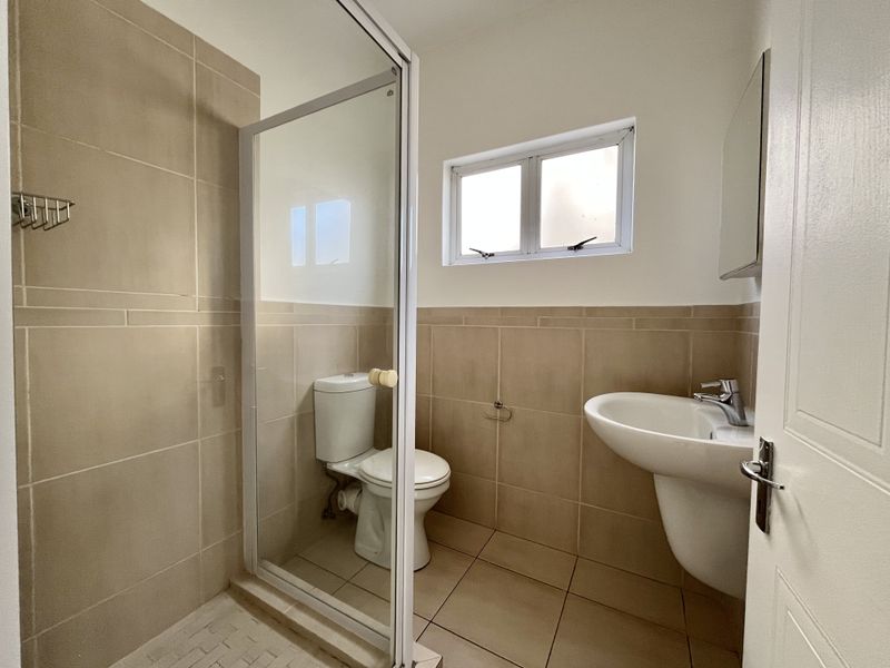 A clean, functional bathroom featuring a glass-enclosed shower, pedestal washbasin, and neutral ceramic tiling throughout.