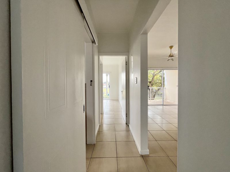 A bright, tiled hallway connecting interior living spaces, featuring a sliding door and direct access to an outdoor balcony area.