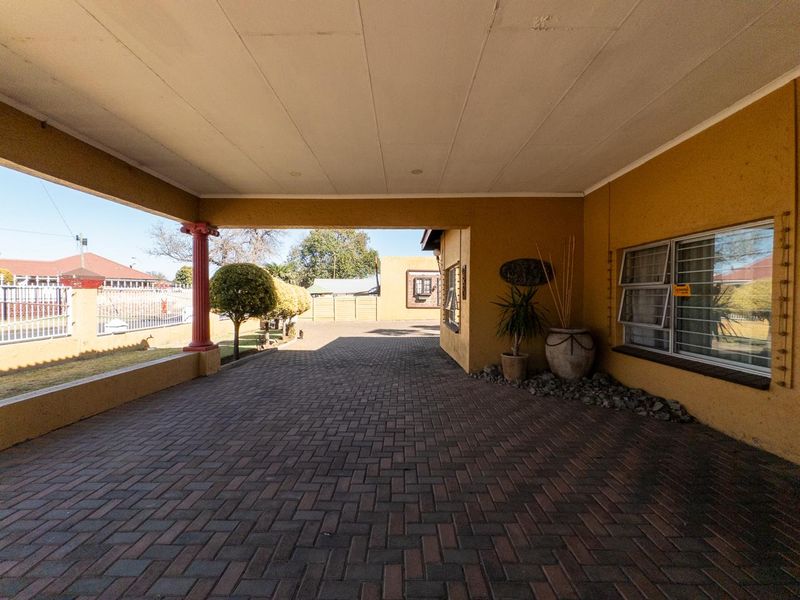 A covered carport area featuring paved driveway, decorative column, and security bars on windows, providing sheltered parking space at the front of the property.
