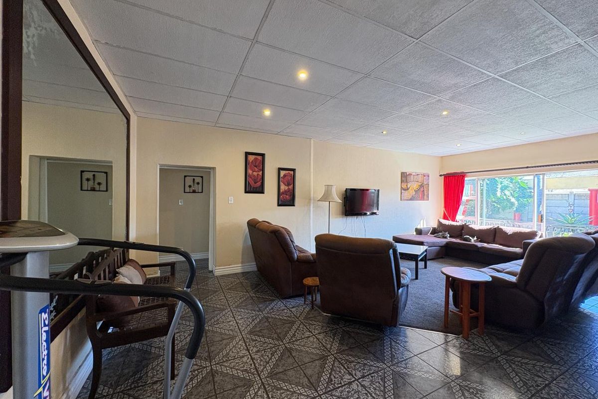 Spacious living room featuring tiled flooring, recessed lighting, and a large wall mirror, with direct access to the outdoor area through sliding glass doors.