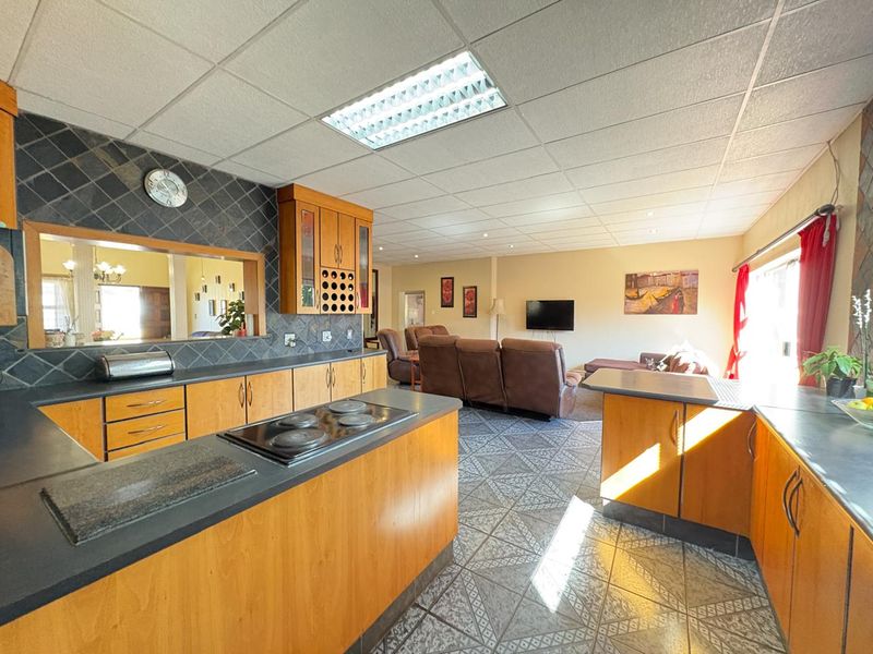 Spacious open-plan kitchen and living area featuring wooden cabinetry, electric hob, and tiled flooring, offering a functional layout with potential for modern updates.