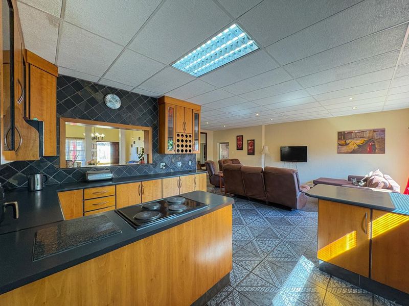 Open-plan kitchen and living area featuring wooden cabinetry, electric hob, tiled flooring, and a functional pass-through window connecting to adjacent spaces.