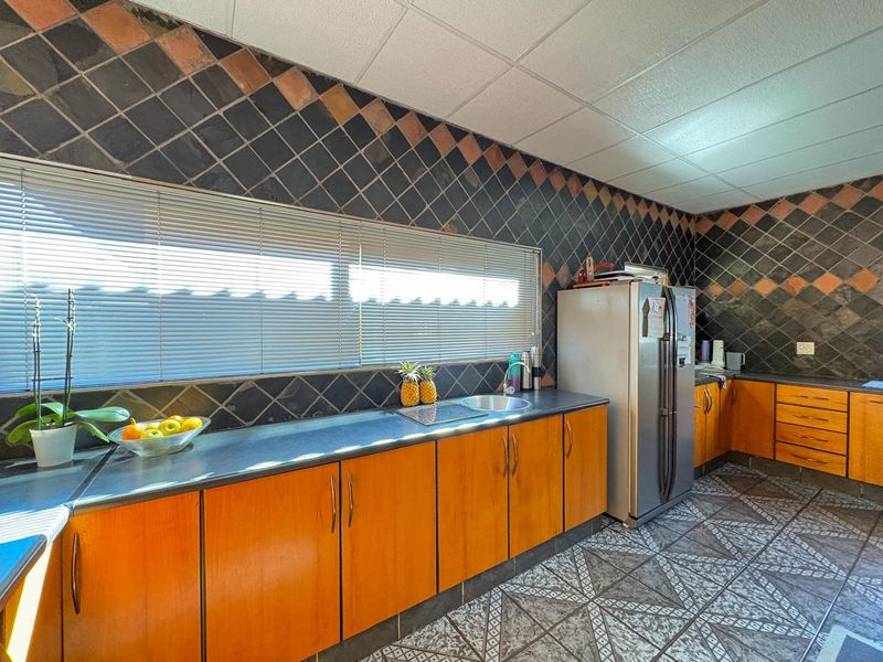 A dated kitchen featuring wood-tone cabinetry, dark tiled backsplash, and patterned floor tiles, offering significant potential for a modern renovation.