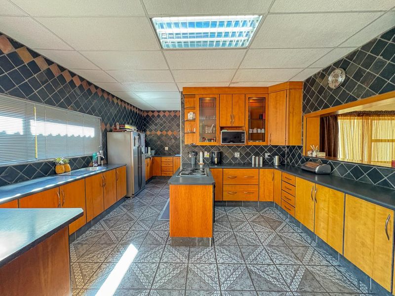 Spacious kitchen featuring extensive wooden cabinetry, a central island with a hob, built-in appliances, and tiled finishes throughout.