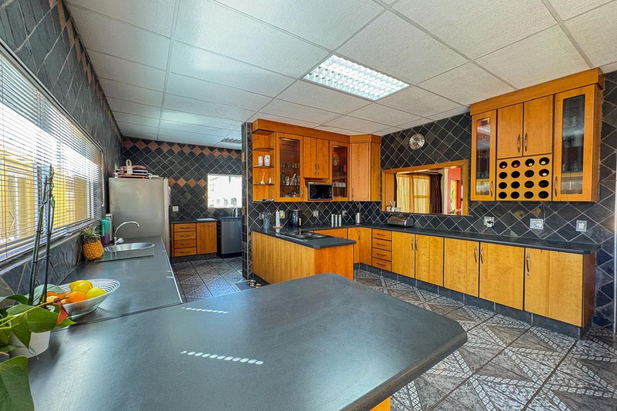 Spacious kitchen featuring extensive wooden cabinetry, dark laminate countertops, tiled backsplash, and functional layout with integrated wine storage.