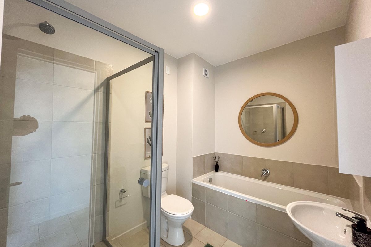 A modern bathroom featuring a glass-enclosed shower, a bathtub with tiled surround, and a pedestal sink in a neutral color palette.