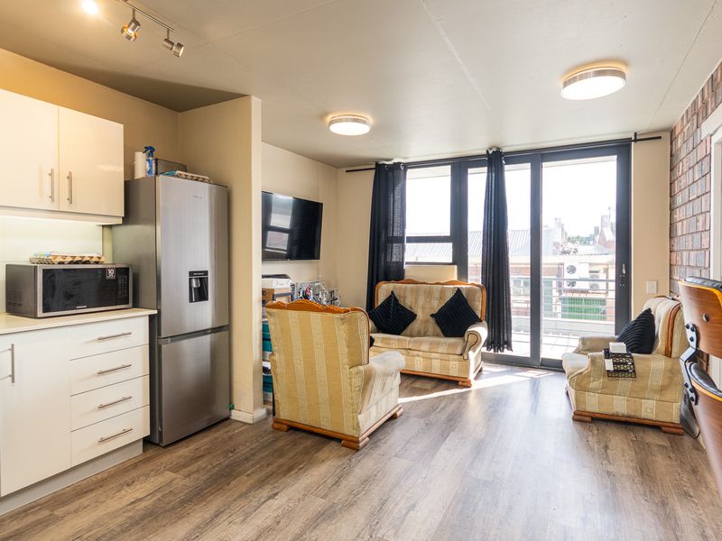 Open-plan living area featuring a modern kitchen with built-in appliances, laminate flooring, and sliding glass doors leading to a balcony.