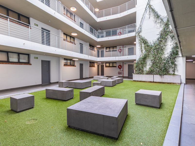 A well-maintained central courtyard area featuring artificial turf, concrete block seating, and multi-level apartment access balconies with metal railings.