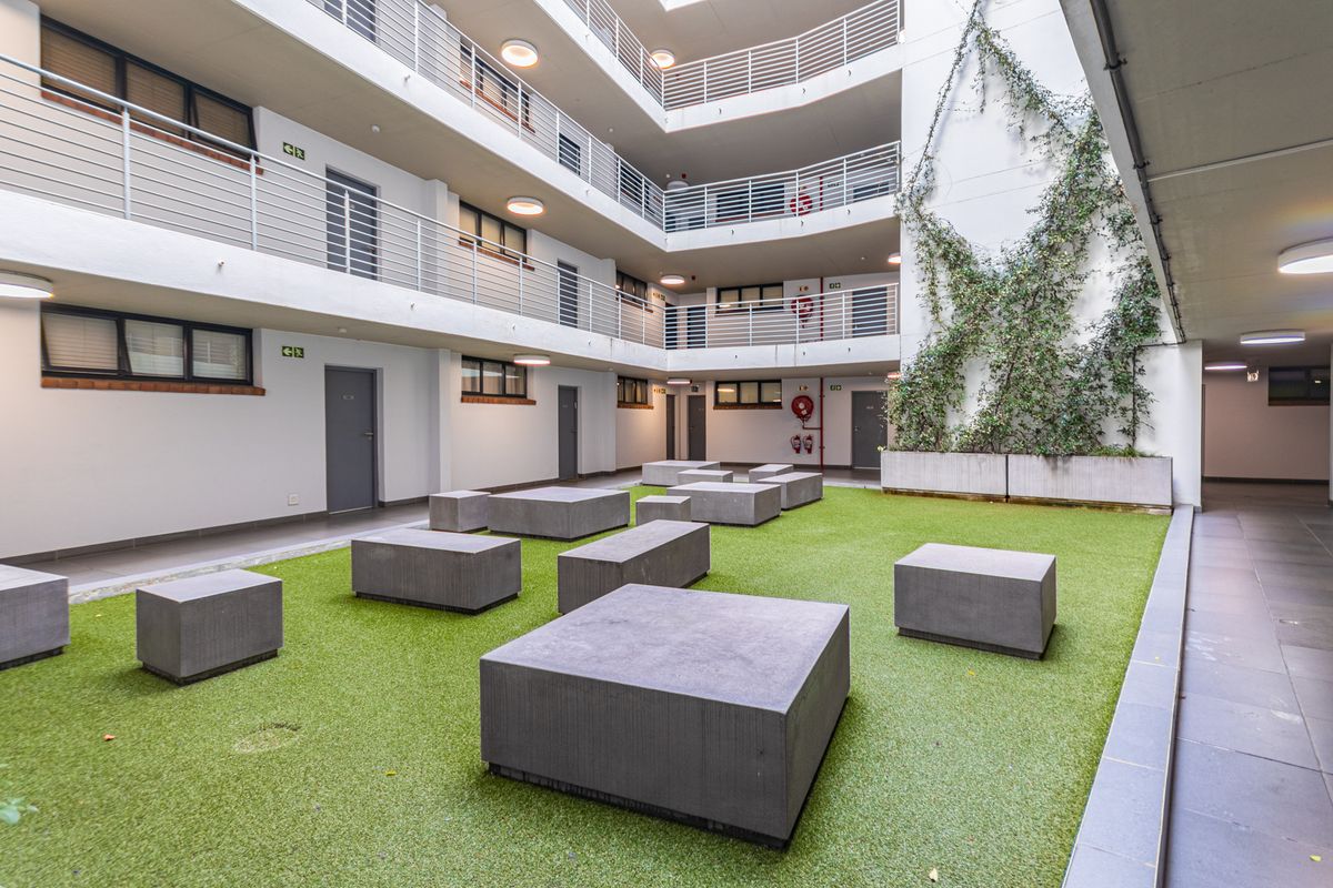 A well-maintained central courtyard area featuring artificial turf, concrete block seating, and multi-level apartment access balconies with metal railings.
