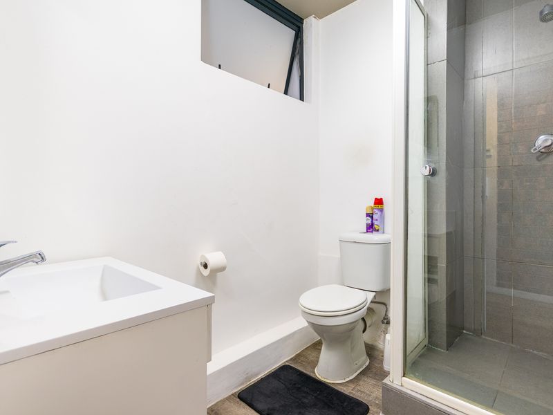 Compact bathroom featuring a vanity basin, toilet, and a glass-enclosed shower with grey tiled walls.