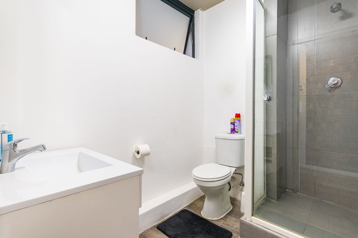 Compact bathroom featuring a vanity basin, toilet, and a glass-enclosed shower with grey tiled walls.