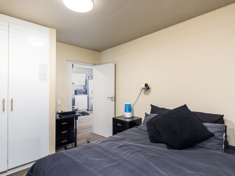 A bedroom featuring built-in wardrobes, laminate flooring, and a view through to the adjacent kitchen area.