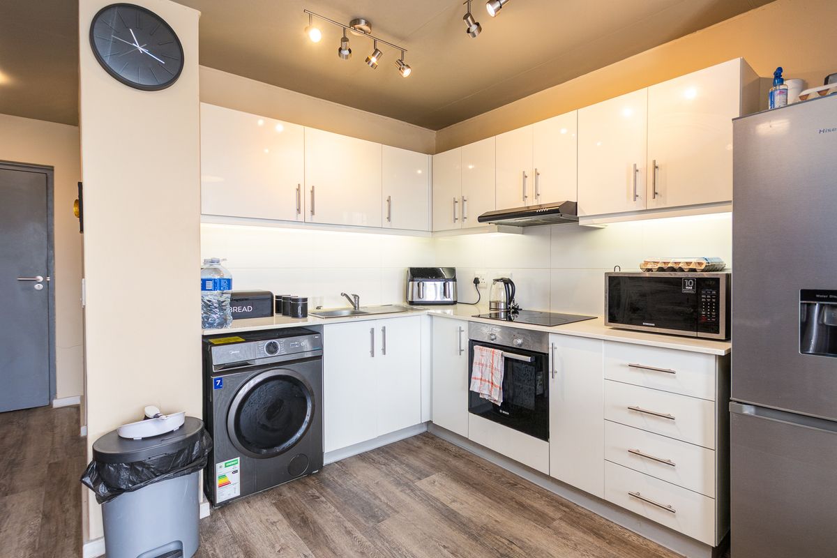 Modern kitchen featuring white high-gloss cabinetry, integrated appliances, laminate countertops, and efficient track lighting in a clean, functional layout.