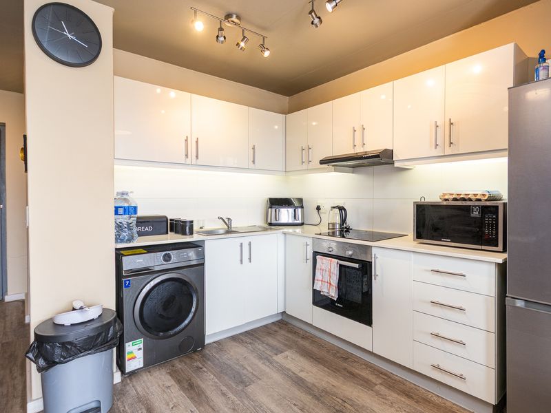 Modern kitchen featuring white high-gloss cabinetry, integrated appliances, laminate countertops, and efficient track lighting in a clean, functional layout.