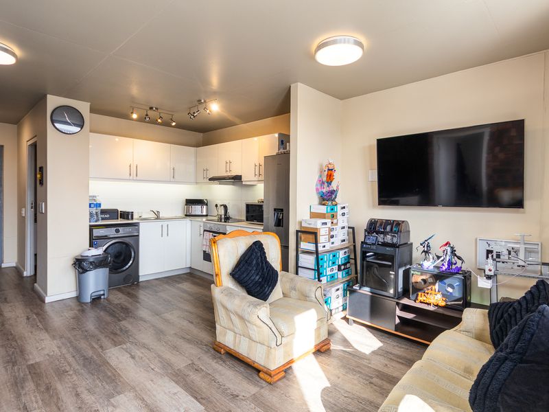 Open-plan living area featuring a modern kitchen with white cabinetry, laminate flooring, and a wall-mounted television, creating a functional and cohesive living space.