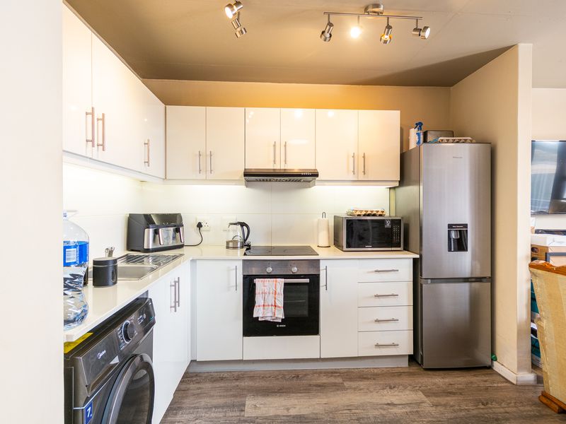A modern, well-maintained kitchen featuring white cabinetry, laminate countertops, integrated oven and hob, and efficient track lighting.