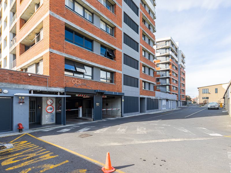 Exterior view of the Obs Court apartment building entrance, featuring a brick facade, secure parking garage access, and paved driveway area.