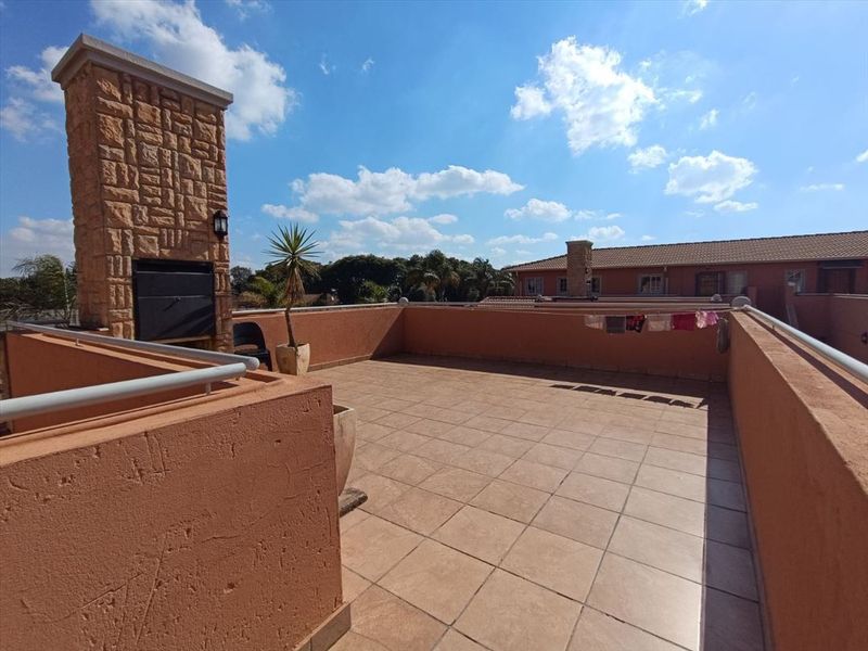 Spacious open-air rooftop balcony featuring a built-in braai with stone cladding and tiled flooring, offering an ideal space for outdoor entertainment.