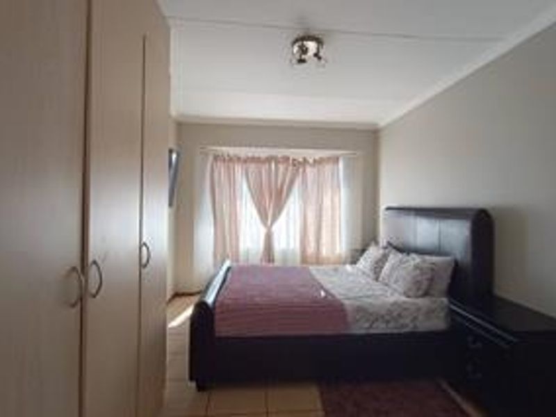 A functional bedroom featuring built-in cupboards, tiled flooring, and a window with natural light.