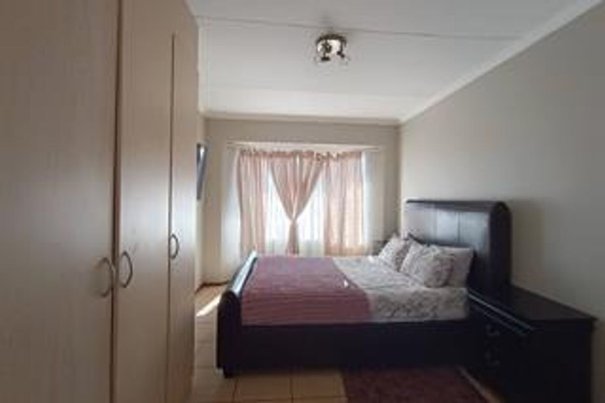 A functional bedroom featuring built-in cupboards, tiled flooring, and a window with natural light.