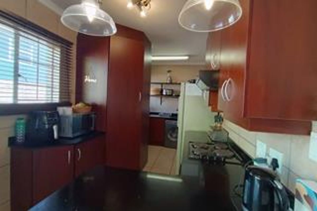 A functional kitchen featuring dark wood cabinetry, granite countertops, a built-in hob, and tiled backsplash, with an adjacent utility area.