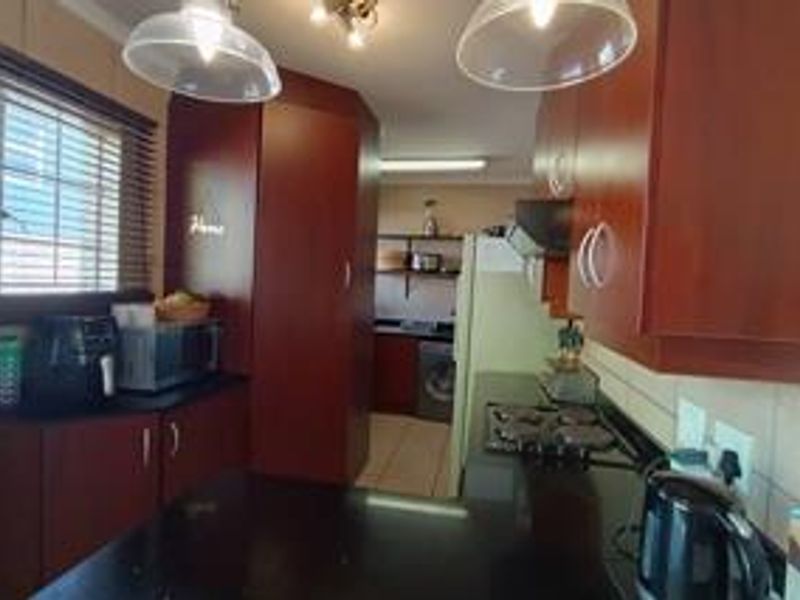 A functional kitchen featuring dark wood cabinetry, granite countertops, a built-in hob, and tiled backsplash, with an adjacent utility area.