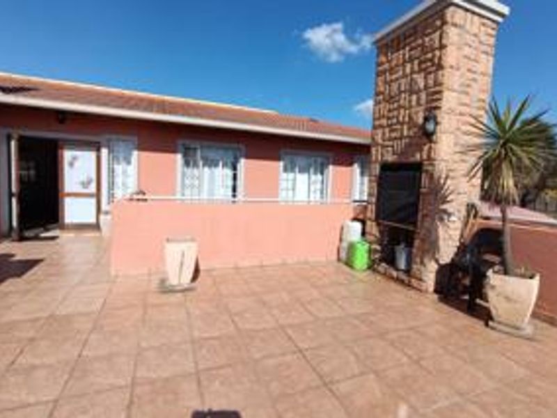 Spacious outdoor patio featuring tiled flooring and a built-in stone-clad braai area, perfect for entertaining.