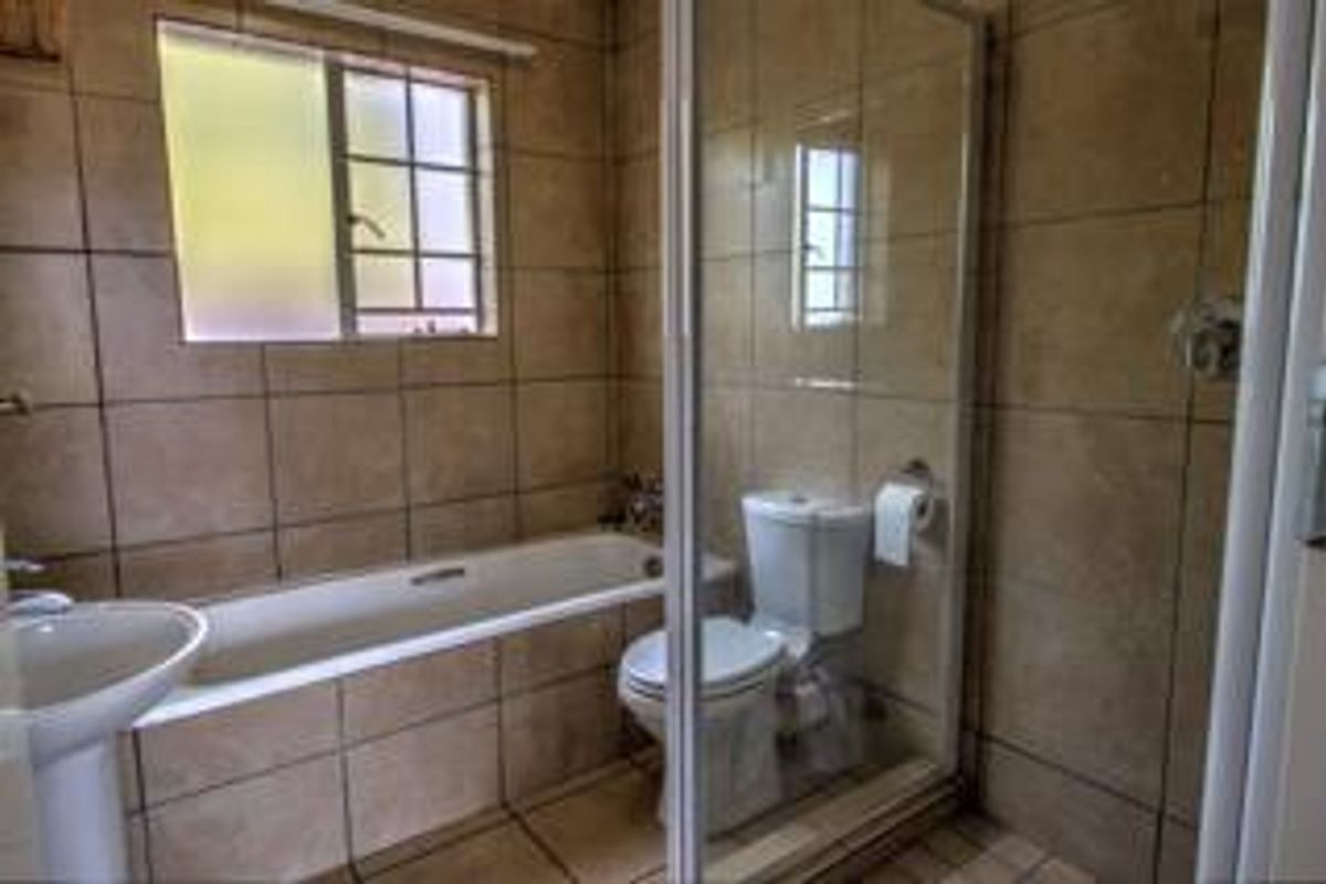 A functional bathroom featuring a pedestal basin, built-in bathtub, and a separate glass-enclosed shower with neutral floor-to-ceiling tiling.