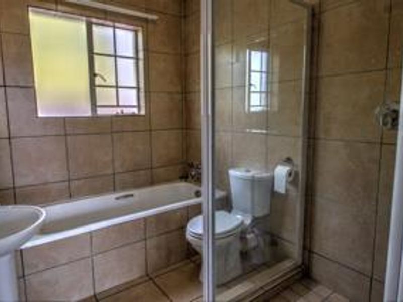 A functional bathroom featuring a pedestal basin, built-in bathtub, and a separate glass-enclosed shower with neutral floor-to-ceiling tiling.