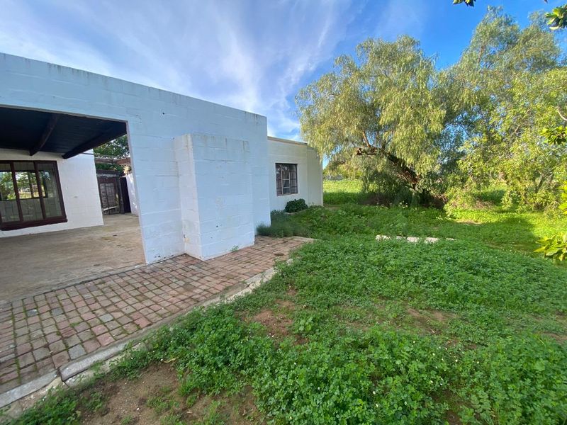 Rear view of the cottage featuring a covered patio area, brick paving, and an expansive garden space requiring landscaping maintenance.