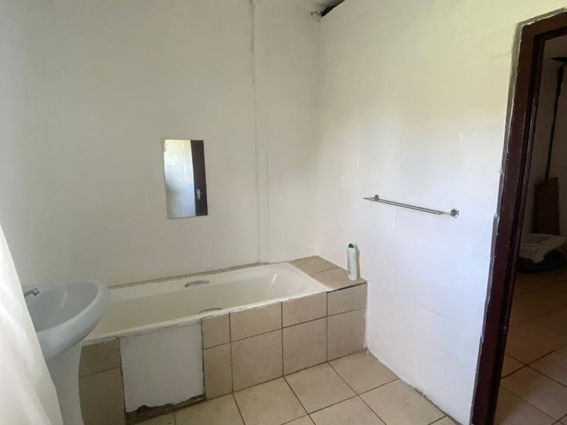 A basic bathroom featuring a pedestal basin and a built-in bathtub with tiled surround, requiring cosmetic updates and repairs to finishes.