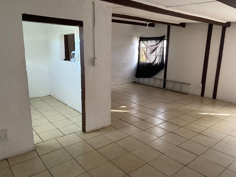 An empty, open-plan living area featuring tiled floors, exposed ceiling beams, and cinder block walls, offering a blank canvas for renovation.