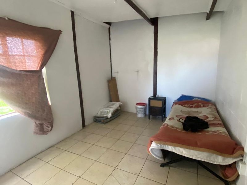 A simple bedroom featuring ceramic floor tiles and exposed ceiling beams, currently in need of cosmetic updates and repairs to the flooring.